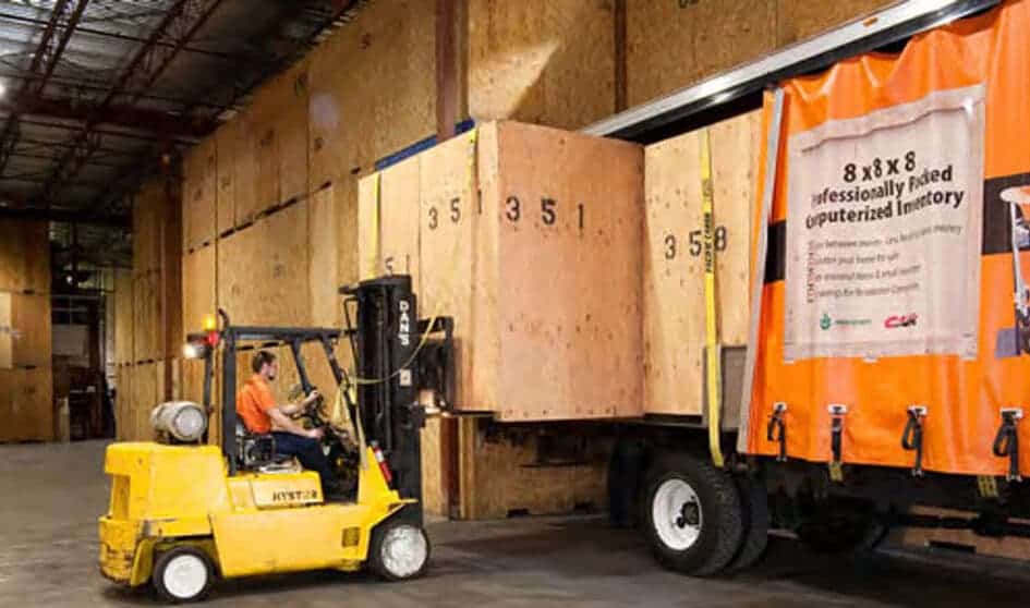 Man driving forklift to move a storage container inside a warehouse facility.
