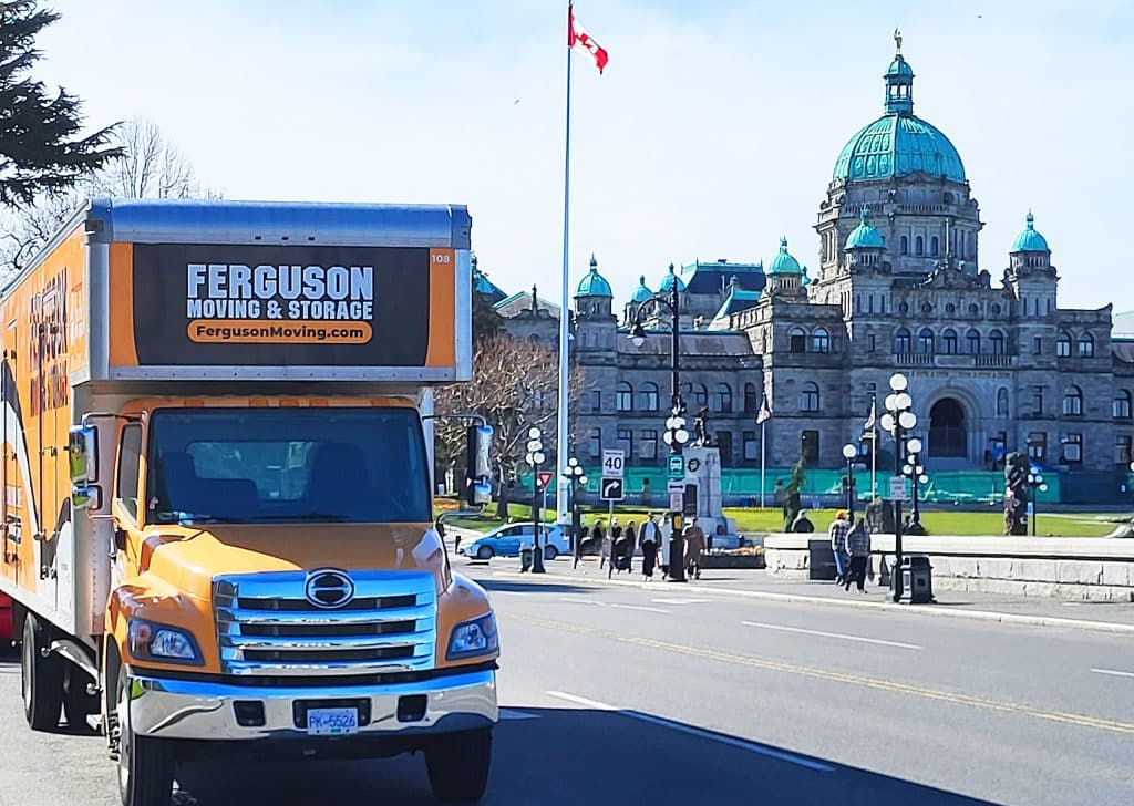 Ferguson Moving truck driving with the Victoria Parliament Building in the background, highlighting services by moving companies in Victoria