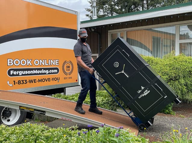 Mover unloading a heavy safe from a truck during a residential move.