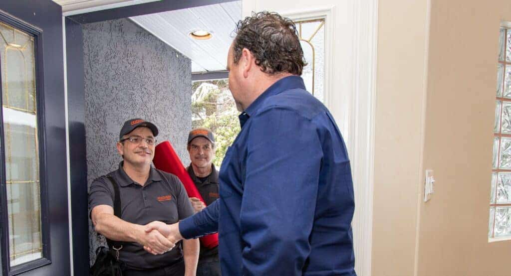 Movers being warmly welcomed by a customer at the door with smiles.