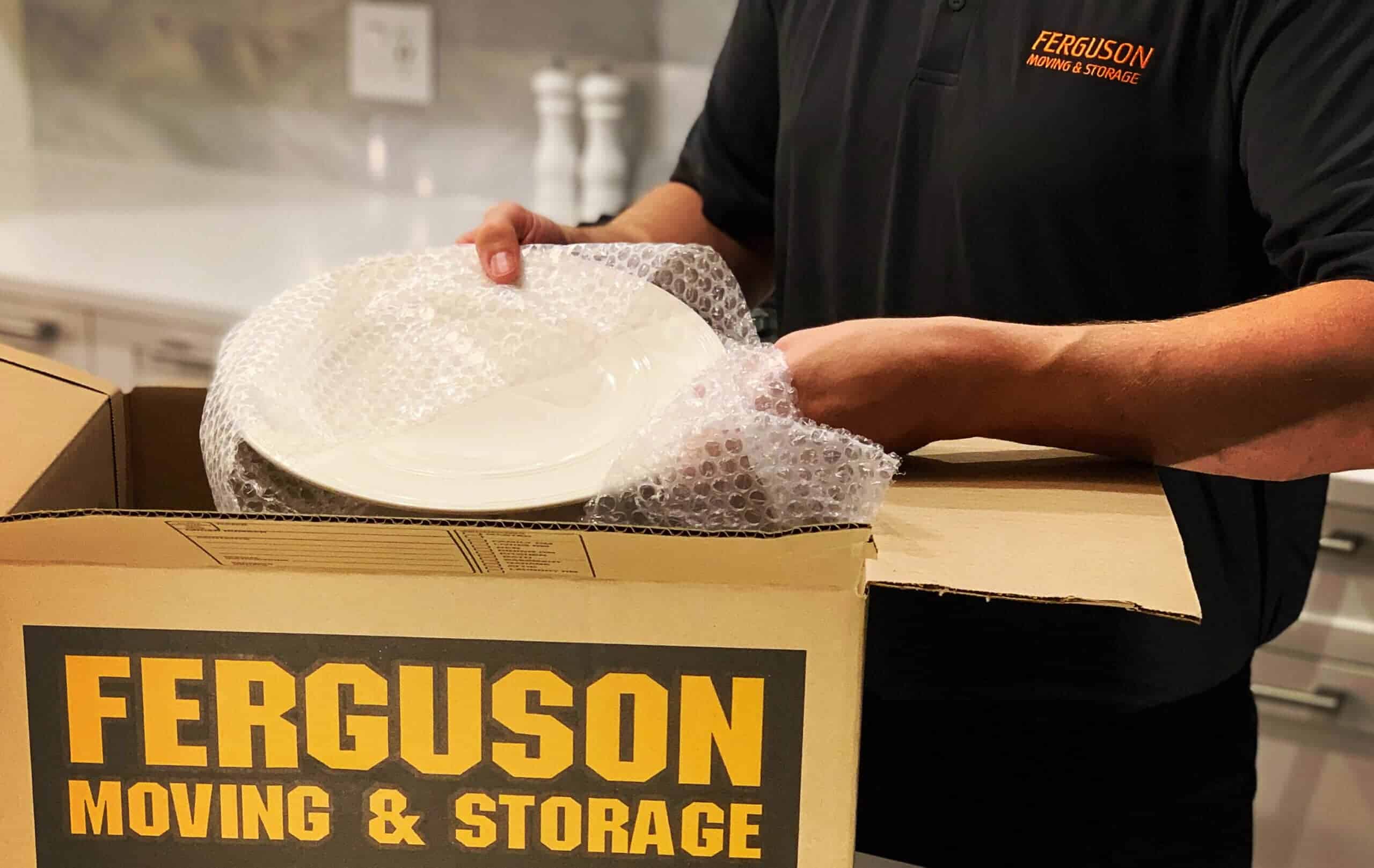 Mover carefully bubble wrapping a plate before packing it into a moving box.